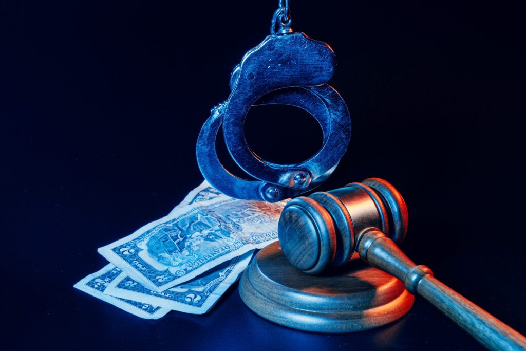 Bribe concept. Dollar banknotes, handcuffs and gavel on dark black table